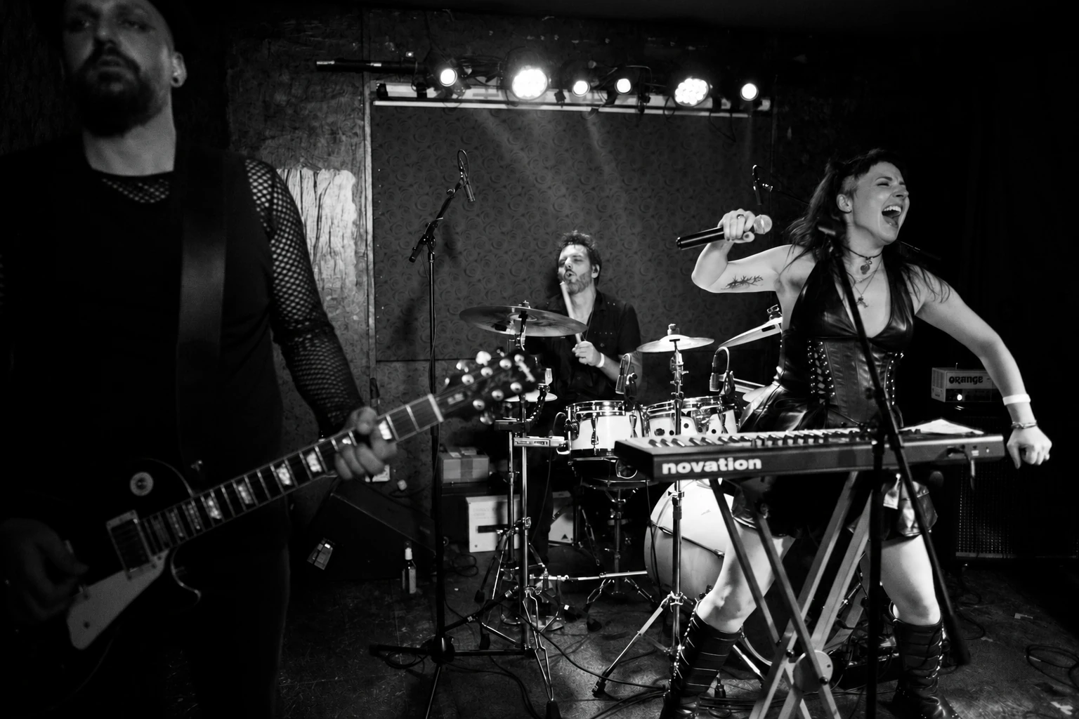 Schwarz-weiß-Aufnahme der Band live im Club mit Rika am Mikrofon, Gitarre und Schlagzeug